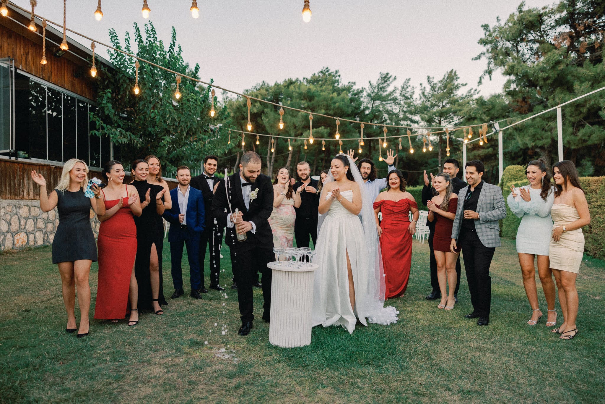 İp fenerlerin altında şampanya açan gelin ve damat ile çevrelerindeki davetliler