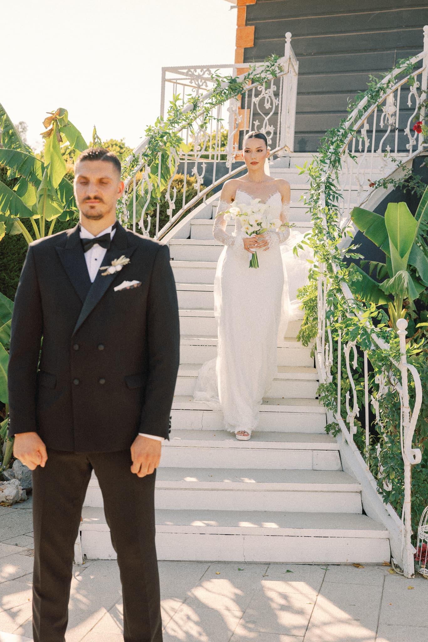 İlk görüşme anı: damat önde beklerken gelin beyaz merdivenlerden iniyor