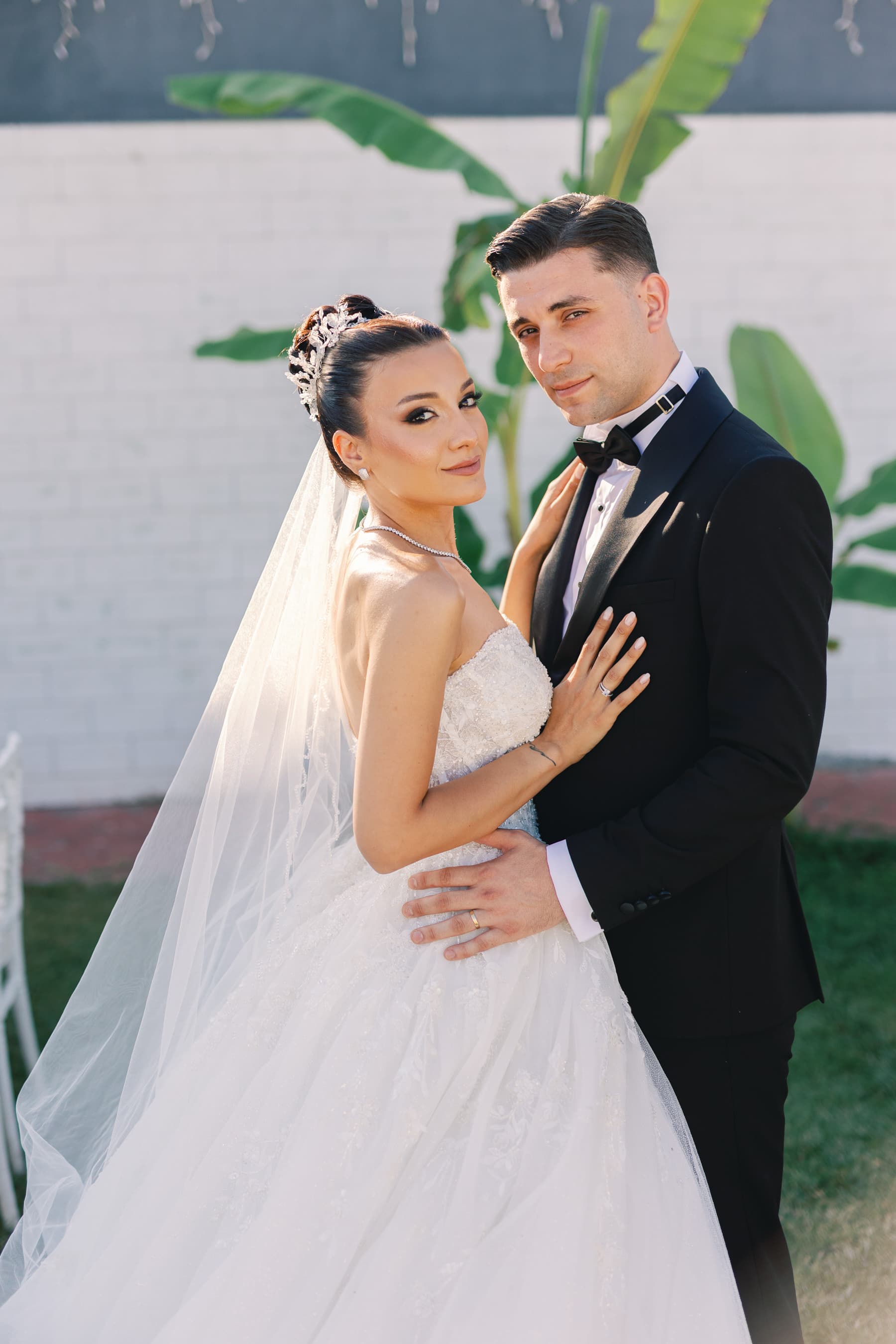 Beyaz duvar önünde birbirine sarılan gelin ve damat portresi